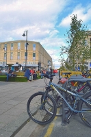 Close up of bikes locked to a bike rack, with people sitting on new seating at Boots Corner in the background