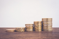 Stacks of pound coins on a wooden surface against a grey background