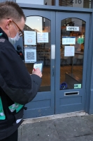 One of our community protection officers standing outside a shop, wearing a mask and green high viz bib, writing in a small notebook