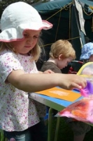 Little girl in a sunhat engaged in a craft activity - sticking feathers to a piece of orange card