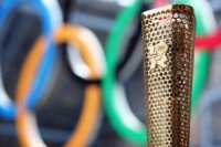 Metallic gold Olympic torch with the Olympic rings in the background (blue, yellow, black, green and red)