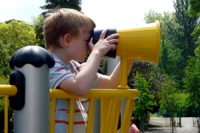 Boy looking through some toy binoculars attached to a yellow climbing frame