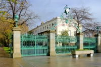 Green painted railings between stone pillars. Elaborate iron arch topped with Cheltenham's coat of arms reads "Pittville Park" in red letters