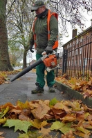 Ubico operative using a leaf blower to clear fallen leaves from a pavement