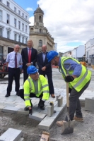 men in high viz jackets and hard hats lay stone slabs on a high street