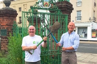 Councillor Max Wilkinson with a representative from Vision21, holding garden tools at the High Street entrance to Sandford Park