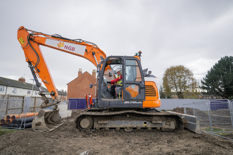 Picture of a digger on building site. The leader of the council is sat inside.