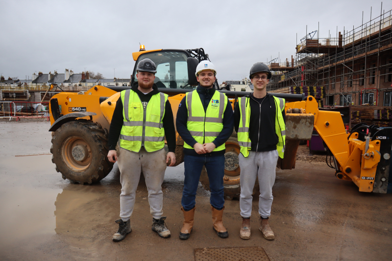 Image of building site, digger behind three people
