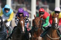 Four jockeys in colourful silks racing astride their horses.
